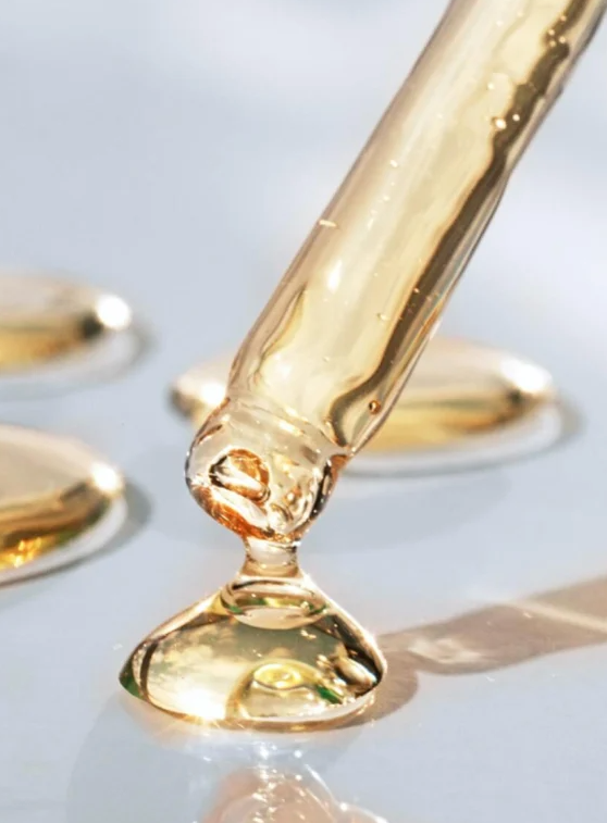 Close-up of a dropper with yellow liquid being dispensed onto a white surface.