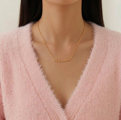 Person wearing a gold necklace with 'Mia' on a plain background