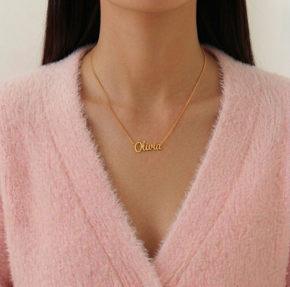 Gold name necklace with 'Olivia' on a person wearing a pink sweater.