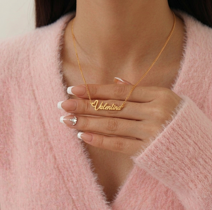 Gold necklace with 'Valentina' pendant worn by a person in a pink sweater.